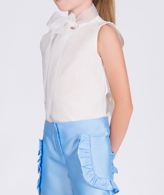 white blouse with a bow on the neck and blue pants with ruffled pockets